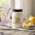 Jar of lavender lemonade candle with a glass of lemon water and lemons on a wooden table.